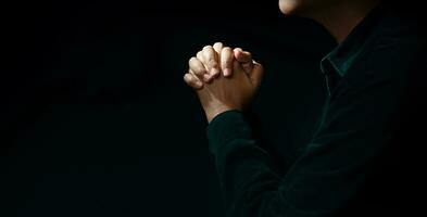 spiritualità, religione e speranza concetto. persona fabbricazione mani per preghiere nel il buio camera. simbolo di umiltà, supplica, credere e fede. buio tono. ritagliata e selettivo messa a fuoco foto