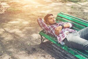 giovane hipster uomo sdraiato su una panchina verde, guardando lontano. foto