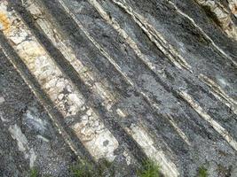 roccia di montagna di pietre di colore grigio, bianco, marrone a strati diagonalmente foto