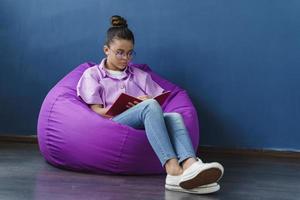 concentrata, carina ragazza seduta in un ottomano viola, studiando foto