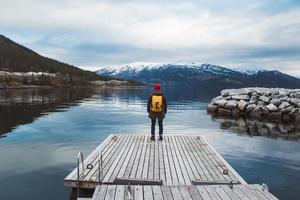 viaggiatore uomo in piedi sul molo di legno sullo sfondo della montagna foto