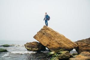 l'uomo viaggiatore con uno zaino si erge su una roccia contro un bellissimo mare foto