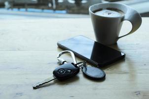 chiave dell'auto e smartphone e tazza di caffè sul tavolo di legno foto