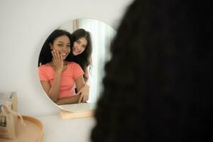 sorridente giovane donna guardare a sua riflessione nel il specchio a casa foto