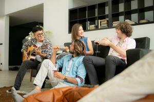 multietnico gruppo di amici avendo divertimento giocando chitarra e cantando insieme a casa foto