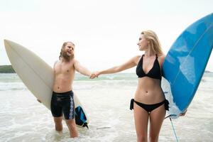 coppia di surfers Tenere mani e guardare a ogni altro su spiaggia foto