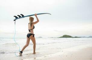 surfer ragazza con sua tavola da surf su il spiaggia. foto