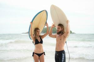 giovane uomo e donna Tenere tavole da surf su loro teste e camminare in il mare per Surf foto