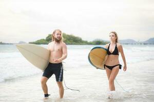 giovane uomo e donna Tenere tavole da surf pronto per camminare in il mare per Surf. foto