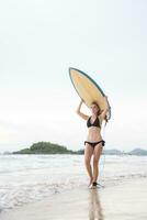 surfer ragazza con sua tavola da surf su il spiaggia. foto