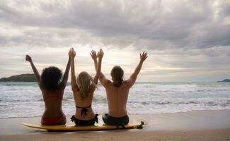 posteriore Visualizza di tre amici seduta su tavola da surf e guardare a mare foto