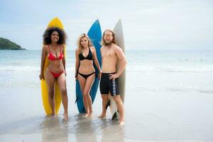 gruppo di amici nel costumi da bagno in posa con tavole da surf su il spiaggia. foto