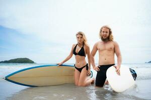 giovane coppia di surfers con tavola da surf su il spiaggia foto