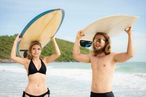 giovane uomo e donna Tenere tavole da surf su loro teste e camminare in il mare per Surf foto