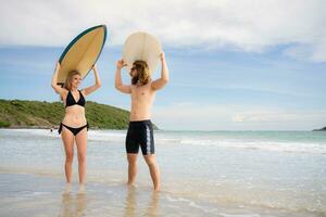 giovane uomo e donna Tenere tavole da surf su loro teste e camminare in il mare per Surf foto