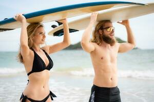 giovane uomo e donna Tenere tavole da surf su loro teste e camminare in il mare per Surf foto