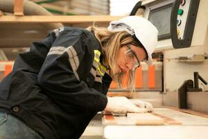 giovane donna lavoratore opera nel un' la lavorazione del legno fabbrica, Lavorando con legna segare e taglio macchine per produrre di legno lenzuola per fabbricazione pallet foto