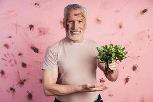 carino, uomo anziano sullo sfondo di un muro rosa sporco con in mano un basilico foto