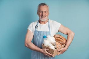 uomo sorridente con i capelli grigi e la barba che tiene un cesto di cibo foto