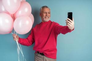 attraente uomo anziano tiene palloncini e prende un selfie