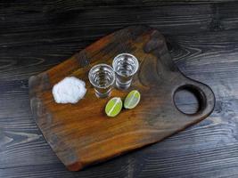 due colpi di tequila argento con lime fresco e sale marino su tavola di legno foto