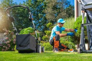 caucasico uomo potatura il suo Giardino dietro la casa giardino impianti Il prossimo per prato falciatore foto