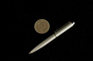 un' penna e moneta su nero sfondo foto