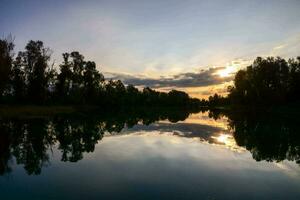 il sole imposta al di sopra di un' lago nel il mezzo di un' foresta foto