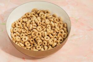 delizioso miele cheerios cereale nel un' ciotola su rosa sfondo. avvicinamento, piatto posizione, copia spazio. prima colazione concetto foto