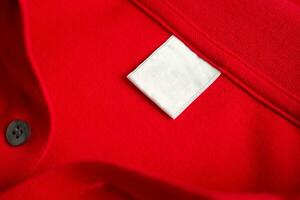 vuoto bianca lavanderia cura Abiti etichetta su rosso camicia tessuto struttura sfondo foto