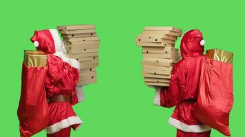 personaggio consegna scatole di Pizza nel studio, in piedi al di sopra di schermo verde con grande mucchio di veloce cibo e Borsa pieno con regali. Santa Claus nel di stagione inverno costume recitazione piace un' fattorino. foto