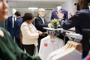 africano americano donna negozio i saldi assistente organizzazione Abiti su stoffa cremagliera mentre Lavorando nel moda memorizzare durante nero Venerdì i saldi. femmina Al dettaglio lavoratore organizzazione capi di abbigliamento su grucce foto