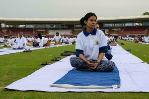 nuovo delhi, India, giugno 21, 2023 - gruppo yoga esercizio sessione per persone a yamuna gli sport complesso nel delhi su internazionale yoga giorno, grande gruppo di adulti frequentando yoga classe nel cricket stadio foto