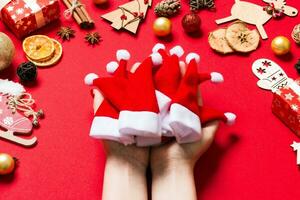 superiore Visualizza di femmina mani Tenere un' pila di Santa cappelli su rosso sfondo. nuovo anno decorazioni. Natale vacanza concetto foto