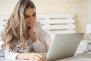 bella donna felice che lavora su un laptop sul letto in casa foto