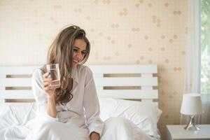 bella donna che beve acqua fresca a letto al mattino foto