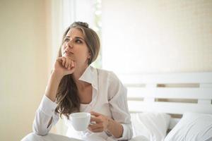 bella donna nella sua camera da letto che beve caffè al mattino foto