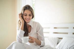 bella donna nella sua camera da letto che beve caffè al mattino foto