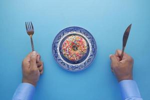 vista dall'alto della mano dell'uomo con coltello e forchetta per mangiare ciambelle foto