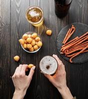 mani di donna che tengono un bicchiere di birra e uno spuntino al formaggio su sfondo nero foto