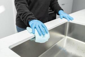 mani in guanti protettivi che puliscono un lavandino moderno con uno straccio