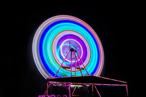 sfocatura movimento di leggero Ferris ruota. lungo esposizione leggero a notte divertimento parco, allegro partire intorno a. foto