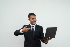 ritratto giovane asiatico uomo d'affari contento con sorridente viso leggere bene notizia, dito puntamento il computer portatile isolato su bianca sfondo foto