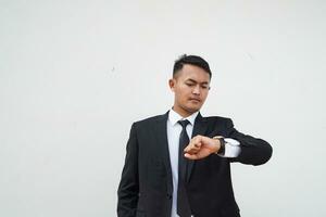 ritratto giovane asiatico uomo d'affari in attesa gesto e Guarda tempo a il orologio , isolato su bianca sfondo foto