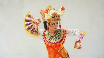 ragazza indossare balinese tradizionale vestito con un' danza gesto su bianca sfondo con -Tenuto in mano fan, corona, gioielleria, e oro ornamento Accessori. isolato balinese ballerino donna ritratto foto