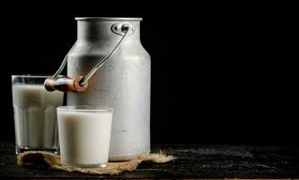 rustico latte nel un' può e un' bicchiere su il tavolo. foto