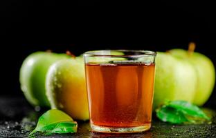 un' bicchiere di verde Mela succo con le foglie su il tavolo. foto