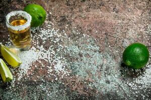 Tequila nel un' tiro bicchiere con sale e fette di fresco lime. foto