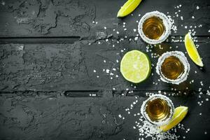 Tequila nel un' tiro bicchiere con sale e fette di fresco lime. foto
