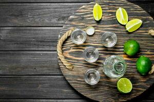 Vodka nel un' tiro bicchiere e un' bottiglia su vassoio con lime. foto